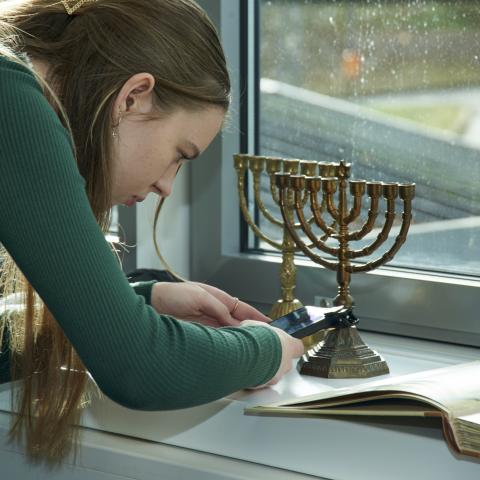 Schülerin fotografiert Menora mit ihrem Smartphone